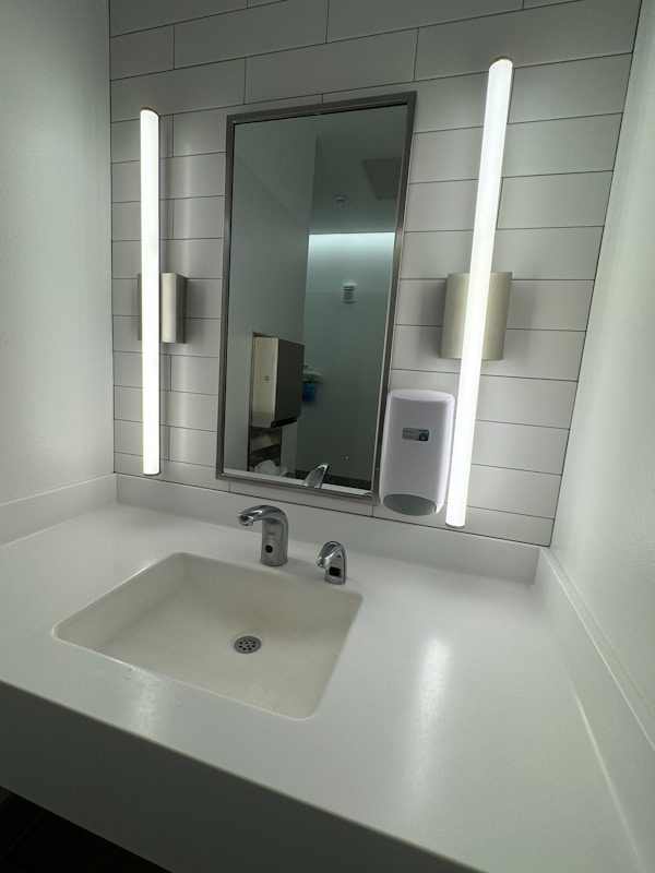A bathroom with a sink, mirror and soap dispenser